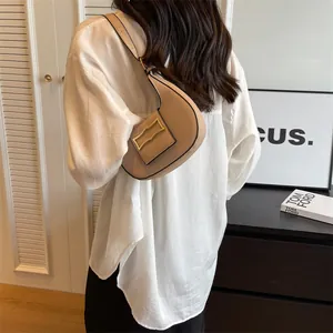 Minimalist beige crescent shoulder bag with gold clasp shown in lifestyle setting