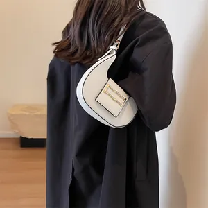 Detail view of white crescent shoulder bag with golden metal buckle on dark coat