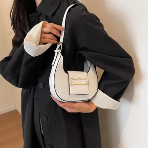 Close-up of white crescent shoulder bag featuring gold arch buckle and adjustable strap
