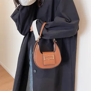 Close-up of brown matte leather crescent hobo bag with gold metal buckle on a model