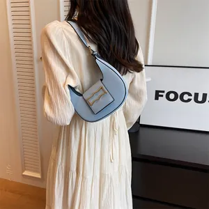 Detail of light blue crescent underarm bag with a gold rectangular metal buckle on a model