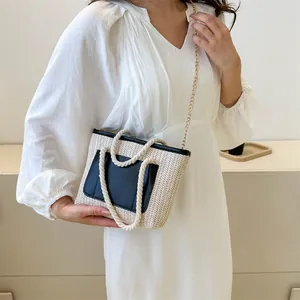 Détail du sac bandoulière en paille tressée avec poche en cuir noir et chaîne dorée