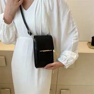 Close-up of a minimalist black leather crossbody phone bag with gold metal trim detailing