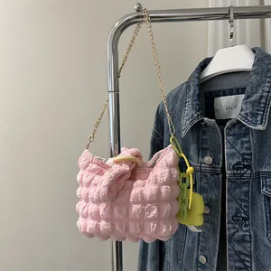 Detail of light pink bubble texture fabric bag with gold chain strap and flower charm
