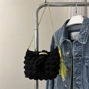 Detail of black textured bubble shoulder bag with gold chain and yellow plush charm