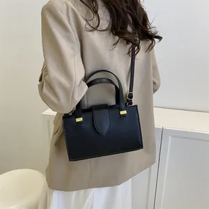 Detail view of black pebble leather square bag with gold hardware worn on beige blazer