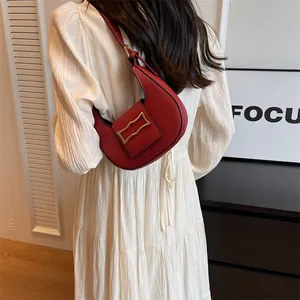Minimalist red crescent leather shoulder bag with gold buckle on a model's white dress