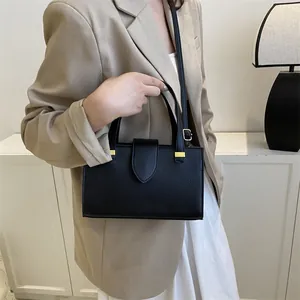 Detail of black lychee grain leather handbag with gold metal hardware on beige blazer