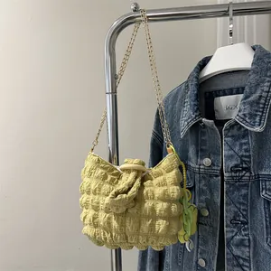 Detail of light yellow popcorn texture shoulder bag with gold chain and green flower charm