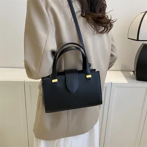 Close-up of a black leather square bag with gold hardware and shoulder strap on a model