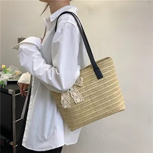Detail of hand-woven straw tote bag with a white lace bow and black leather straps