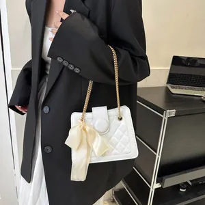 Detail of white quilted handbag with silk bow and gold chain on model in office