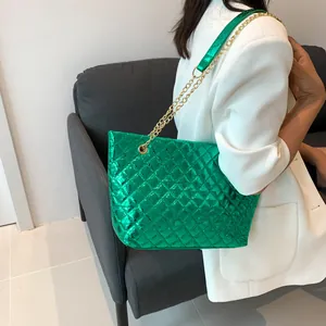 Green metallic quilted tote bag with golden chain strap worn with white suit