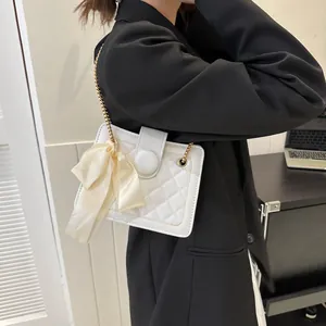 Detail of white quilted crossbody bag with golden chain and cream silk bow accent