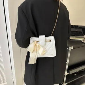 Detail of white quilted handbag featuring a large satin bow and golden chain strap
