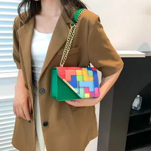 Detail of colorful Tetris style crossbody bag with gold chain and green leather side