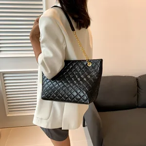 Detail of black quilted tote bag with golden chain strap on model in white blazer