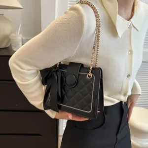 Detail of black quilted chain bag with large silk bow decoration and golden strap