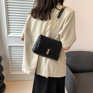 Detail of black quilted chain bag with gold metal clasp worn by a model in a casual setting