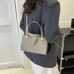 Minimalist grey leather small square handbag with golden hardware shown on a model