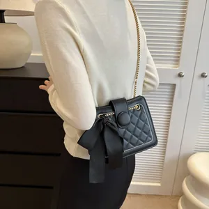 Close-up of quilted black crossbody bag featuring a satin bow and gold chain strap