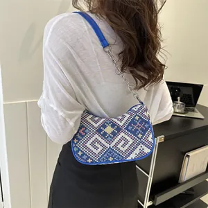 Detalle de bolso bohemio tejido con patrones geométricos azules y correa de cadena fina
