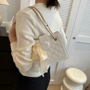 White quilted crossbody bag with gold chain and silk bow shown on a female model