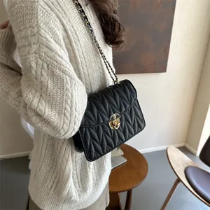 Detailansicht einer schwarzen Stepptasche mit Goldschloss auf beigem Strickpullover