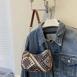 Detalle de bolso medialuna tejido con motivos geométricos y correa de cadena y piel