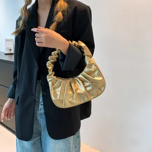 Close-up of golden pleated cloud bag with metallic finish held by a model in a black suit