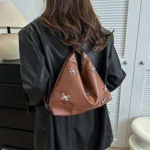 Detail of a brown triangular tote bag with silver butterfly charms on a leather jacket
