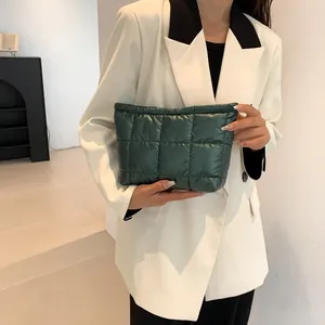 Close-up of quilted dark green puffy clutch bag held by model in white blazer