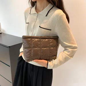 Detail of a brown quilted puffer clutch bag with shiny finish and zip closure held by model