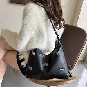 Close-up of black leather underarm bag with silver butterfly buckles and glossy texture