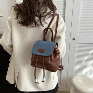 Detail of mini backpack featuring brown PU leather and blue denim patchwork with drawstring