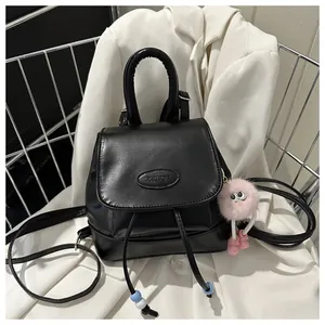 Detail of black leather backpack with drawstring closure, brand logo and pink plush charm