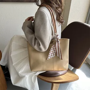 Dettaglio della borsa tote beige con foulard a scacchi sul manico indossata da una modella