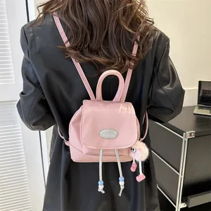 Pink leather mini backpack with plush charm worn by model over a black jacket