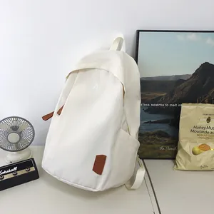 Detail of white nylon backpack featuring a minimalist embroidered A and leather label