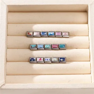 Macro shot of stainless steel Italian charm links with ocean theme icons on velvet tray