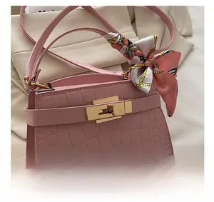 Macro view of pink crocodile embossed handbag with golden lock and decorative scarf detail