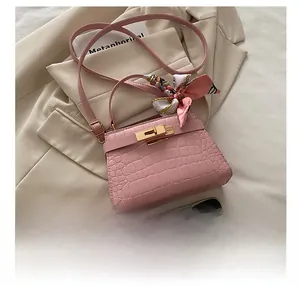 Pink croc-effect trapezoid handbag with gold lock and silk scarf detail next to a phone
