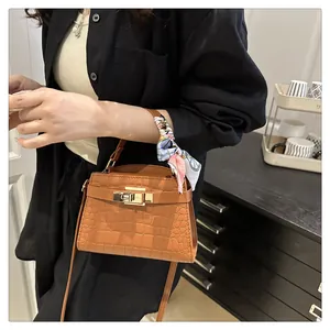 Detail of caramel crocodile pattern handbag with gold clasp and decorative silk scarf
