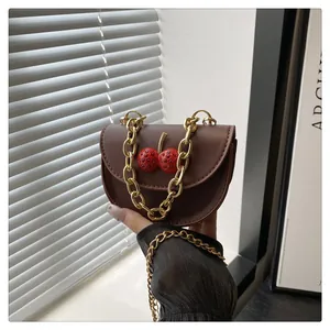Dettaglio della borsa in pelle marrone con decoro a ciliegia e catena d'oro spessa