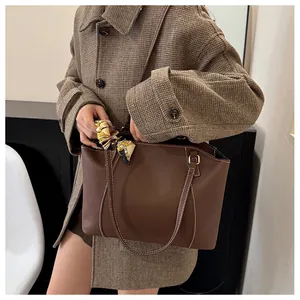Détail d'un sac cabas marron foncé avec surpiqûres contrastées et foulard en soie décoratif