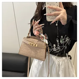 Close-up of beige crocodile pattern bag with gold clasp and silk scarf handle detail