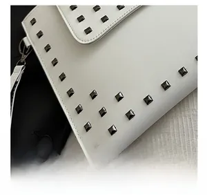 Detail of white envelope clutch showing black square studs and precision stitching