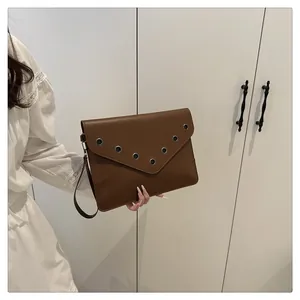 Detailed view of brown leather envelope clutch bag featuring metal eyelet trim and wristlet