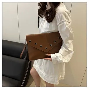 Detail view of brown leather envelope clutch with silver eyelets and wrist strap