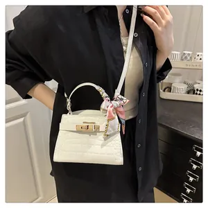 Detail of white crocodile pattern handbag with gold hardware lock and decorative scarf